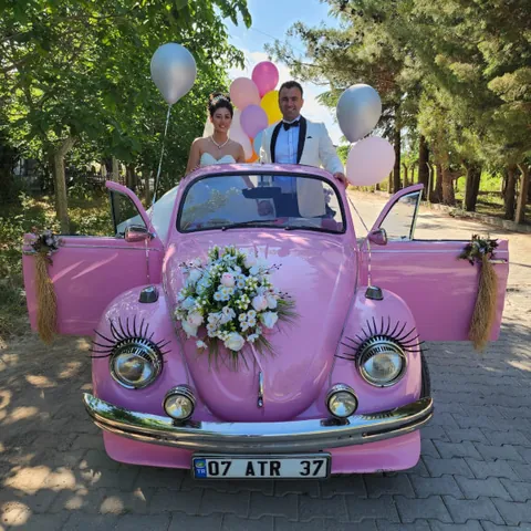 Kaputunda beyaz ve krem çiçek buketi olan pembe cabrio Vosvos gelin arabası, arkada gelin ve damat